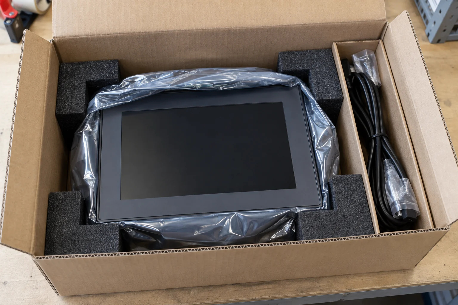 Protective packing example showing an HMI panel with foam corner supports and a separate cable compartment, ready for packing.